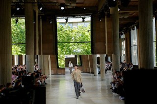 【Hermès 2026春夏男装秀】巴黎 2026 春夏男装周 Hermès 秀场，模特们正在展示品牌男装艺术总监 Véronique Nichanian 的新一季时装作品，耶纳宫。本季 Hermès 男装作品以「都市夏日」（Summer in the city）为主题，设计师选择石灰泥、咖啡、焦糖、淡灰褐、牛皮纸色等中性色实现「视觉降温」，并通过镂空编织工艺为皮夹克、衬衫、长裤等单品注入呼吸感，搭配流苏菱形巾、绳编底露趾凉鞋、帆布手袋等配饰，营造轻盈流动的悠然夏日氛围。 source